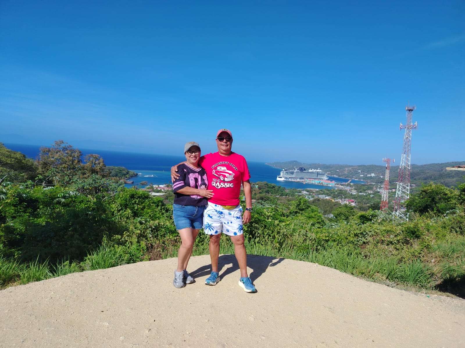 Couple at a Roatán lookout with a cruise ship docked in the bay behind them