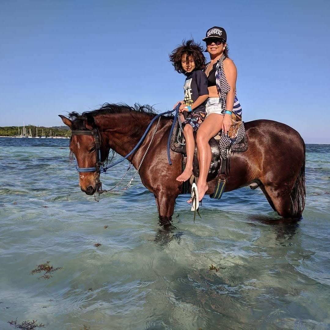 Mother and son horseback riding in the shallow turquoise sea of Roatán